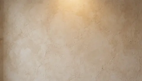 Close-up of a rustic beige stucco wall texture with warm lighting, providing a neutral and cozy background suitable for commercial text overlays.