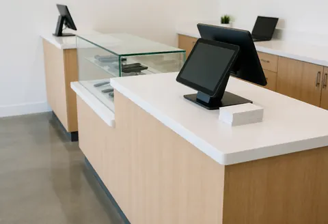 Cash register and glass shelf in a mobile phone repair store with polished concrete floor and light wood furniture.