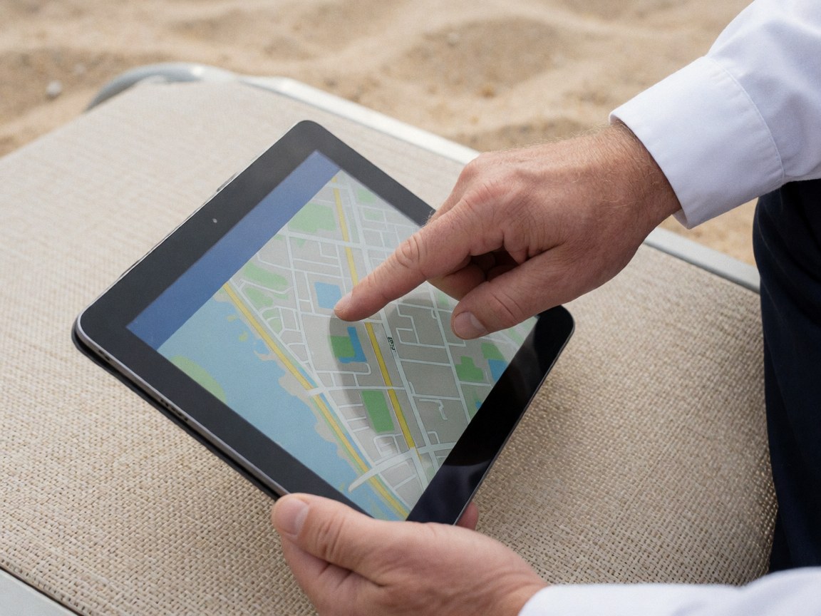 Close-up of a hand interacting with a digital map displayed on a black tablet resting on a beige beach lounge chair, highlighting beach club reservation details.