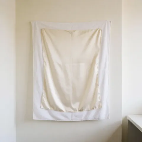 Dry white silk clothing resting on a white towel against a warm-colored wall with natural lighting in a clean minimalist scene
