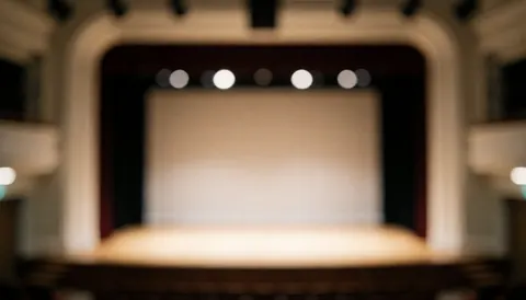 Empty theater stage with warm lighting and proscenium arch, blurred background suitable for text overlay in theater workshops