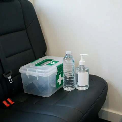 First aid kit, water bottle, and hand sanitizer placed on a black car seat against a white wall for ride-hailing drivers.