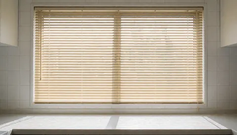 Lowered wooden insulation blind on a kitchen window with white tiles, natural light, and a clean surface