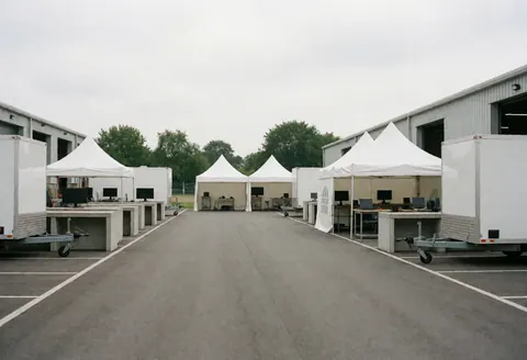 Empty industrial courtyard featuring white tents, work tables, and monitors ready for operations
