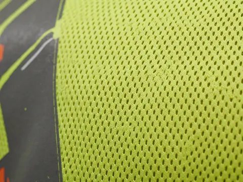 Macro detail of neon yellow safety mesh fabric with a printed border, showcasing high-quality industrial textile construction for business use.