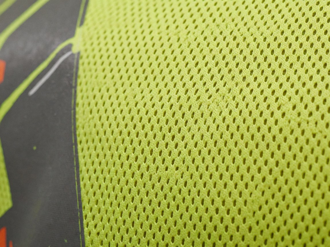 Macro detail of neon yellow safety mesh fabric with a printed border, showcasing high-quality industrial textile construction for business use.