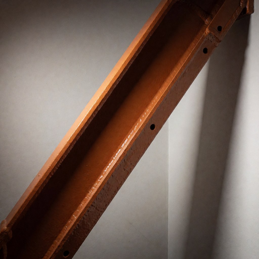 Close-up of an industrial orange steel bolt featuring visible screw holes and welds against a gray background