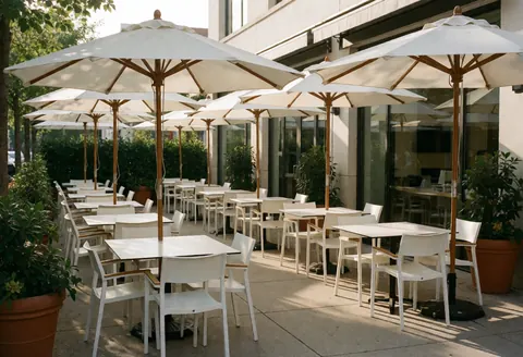 Empty theme park patio featuring white tables, umbrellas, and potted plants illuminated by warm sunset light.