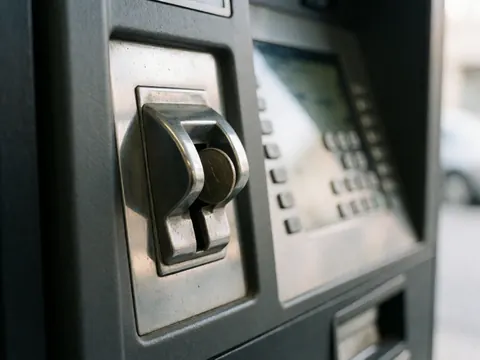 Detail shot of a parking meter with a metal coin partially inserted into the slot, showing the keypad and display screen in the background