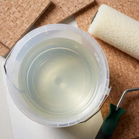 Close-up view of a foam roller and bucket of clear sealer placed on a cork floor surface for installation purposes