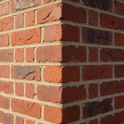 Detailed view of a red brick wall featuring well-applied mortar and a vertical corner illuminated by sunlight, suitable for masonry business use.