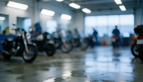 Wet workshop floor reflecting overhead lights with blurred silhouettes of people and parked motorcycles in the background