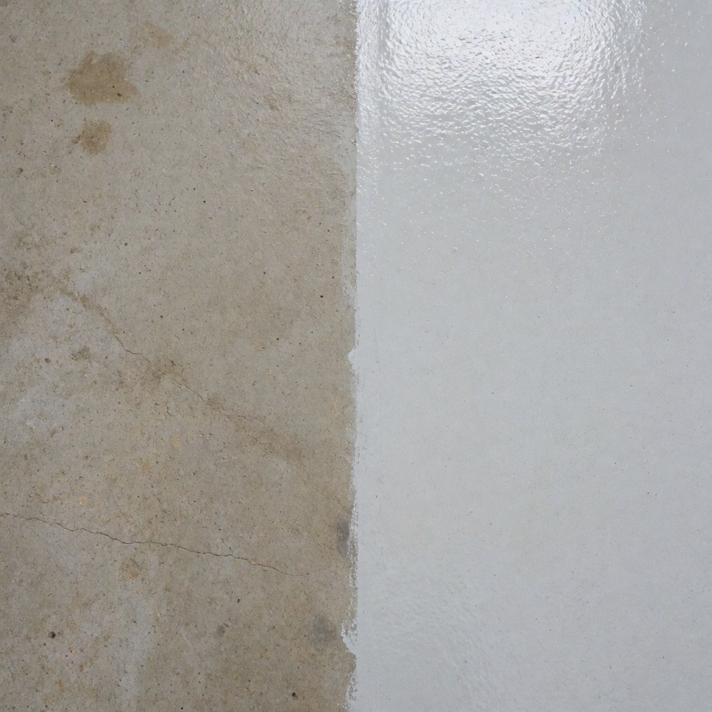 Close-up view of an industrial concrete wall showing a clear contrast between a dirty section and a thoroughly cleaned area after professional cleaning.