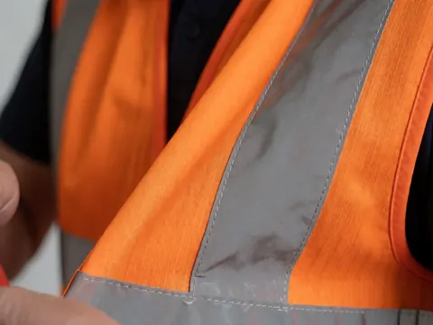 Close-up view of an orange reflective vest showing stitching and metallic reflective strips for outdoor safety gear