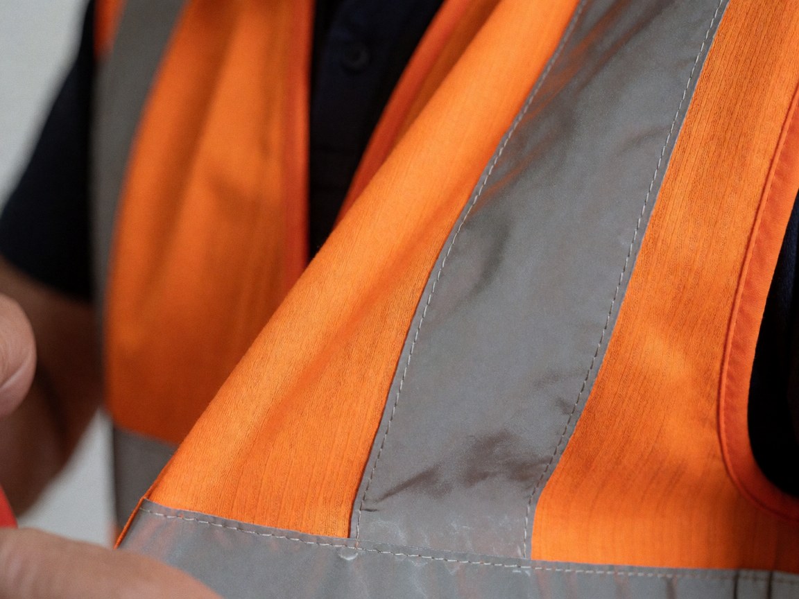 Close-up view of an orange reflective vest showing stitching and metallic reflective strips for outdoor safety gear