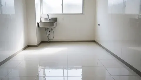 Clean professional kitchen area featuring a stainless steel sink, glossy white tile floor, and a high window letting in natural daylight.