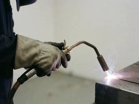 Close-up of a gloved hand holding an arc welding torch while working on metal in an industrial workshop setting