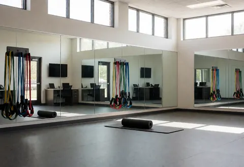 Empty training room with mirrors, resistance bands, and foam rollers on rubber flooring, ideal for a golf instructor.