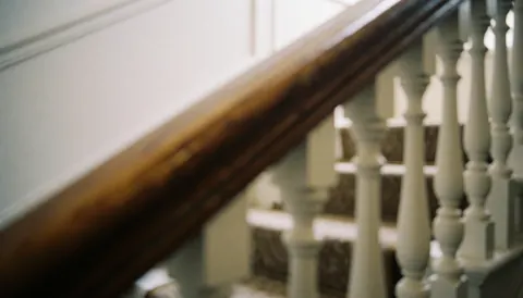Close-up of a polished wood handrail with white balusters on a staircase, suitable for furniture restoration text backgrounds