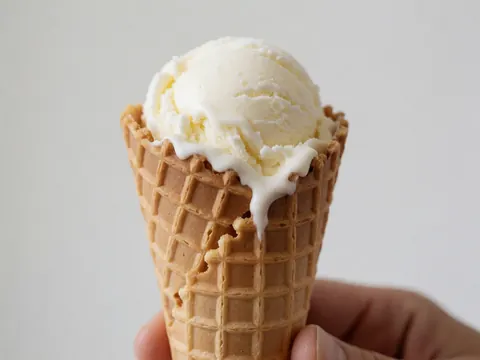 Melting vanilla ice cream served in a waffle cone held by a hand against a white background, suitable for dessert or resort marketing.