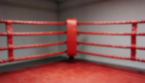 Blurred boxing ring background featuring red ropes and posts against neutral walls and a red floor, suitable for training text overlays