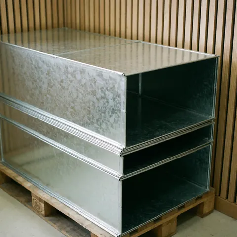 Stacked galvanized metal ducts on a wooden pallet with slat walls and natural lighting for metal stamping business