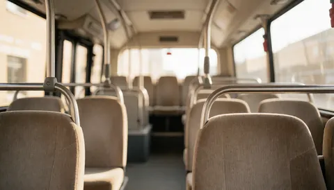 Interior view of a tour bus featuring beige seats and metal handrails with warm lighting and a blurred background suitable for text overlay