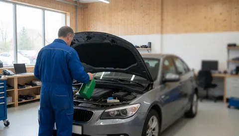 Mechanic adding coolant to a car with the hood open in a workshop with wooden walls and natural light.