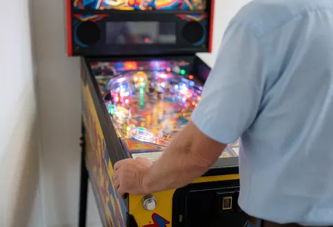 Close-up of an adult's hands on the buttons of a lit pinball machine in an arcade setting