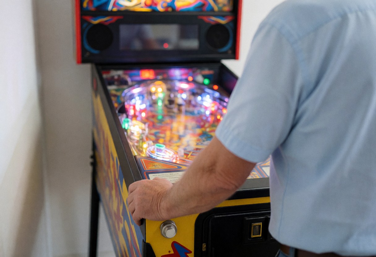 Close-up of an adult's hands on the buttons of a lit pinball machine in an arcade setting