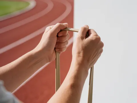 Close-up detail of hands gripping a resistance band on an outdoor athletic track during a flexibility and physical training session