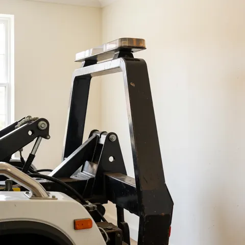 Compact towing unit with hydraulic system and black metal frame mounted on the rear of a white pickup truck in a well-lit workshop.