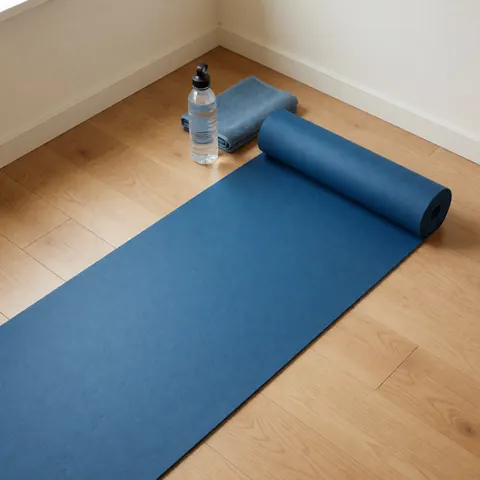 Unfolded blue yoga mat on light wood flooring with a water bottle and blue towel in the corner for home workouts