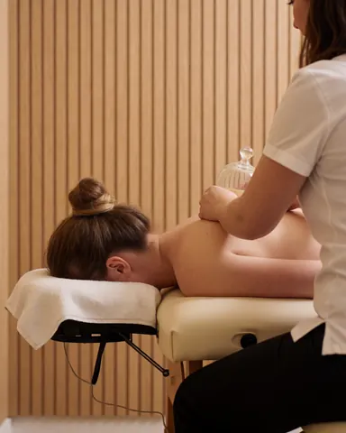 Therapist placing glass cups on a client's back while they lie on a treatment table in a spa with wooden walls