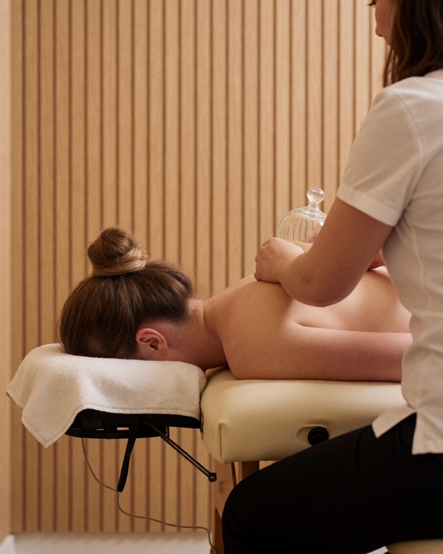 Therapist placing glass cups on a client's back while they lie on a treatment table in a spa with wooden walls