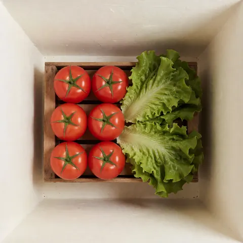 Top view of a wooden crate filled with fresh red tomatoes and crisp green lettuce leaves, ideal for product catalogs and marketing materials.