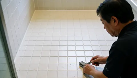 Man repairing grout in bathroom with visible floor and walls, copy space