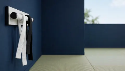 White and black martial arts belts hanging on a wooden rack in a dojo with tatami mats and a dark blue wall