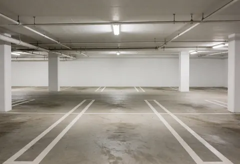Empty covered parking garage with marked concrete floors, white columns, and fluorescent lights, ideal for parking lots.