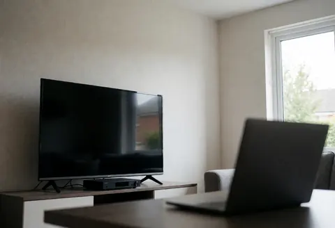 Modern living room featuring a large TV and satellite receiver on a shelf, natural light, minimalist furniture, and smooth walls.