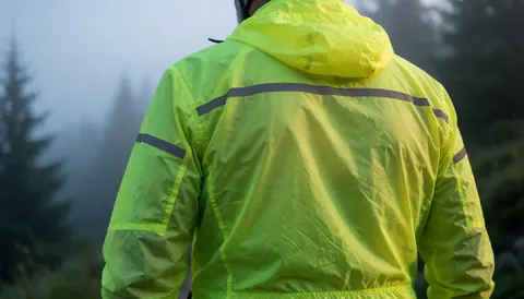 Cyclist wearing a yellow reflective jacket on a misty mountain trail at dawn, suitable for a cycling business website hero section