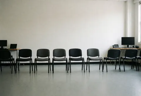 Black chairs lined up against a white wall with computers on tables in a dance studio ready for auditions
