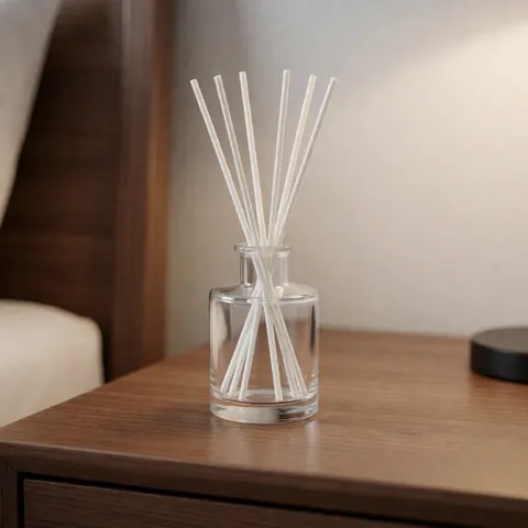 Glass jar aroma diffuser with white reeds placed on a wooden nightstand, suitable for bedroom or living room decor.