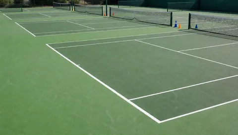 Three green acrylic tennis courts with white boundary lines and nets, suitable for a professional tennis facility.