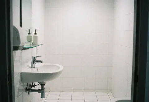 Clean modern bathroom featuring a chrome faucet, white walls, and a glass shelf, suitable for commercial food business use.
