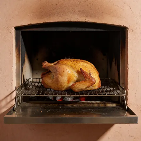 Golden roasted chicken on metal grate inside charcoal oven with clay walls, ideal for poultry business