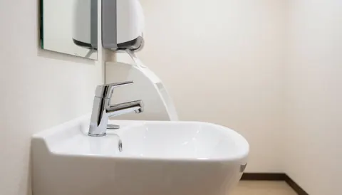 Close-up view of a clean white bathroom sink featuring a shiny chrome faucet and a mirror reflection, suitable for commercial food service environments.