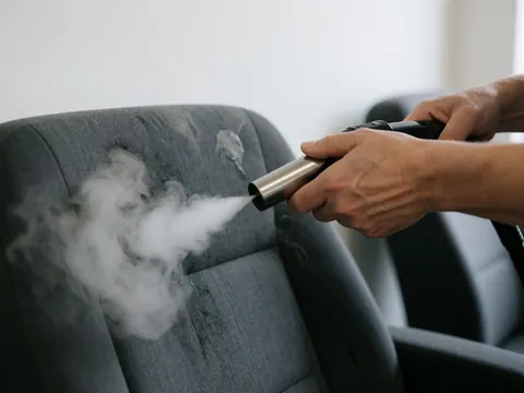 Steam nozzle cleaning gray car seat with white vapor, professional auto detailing service in action