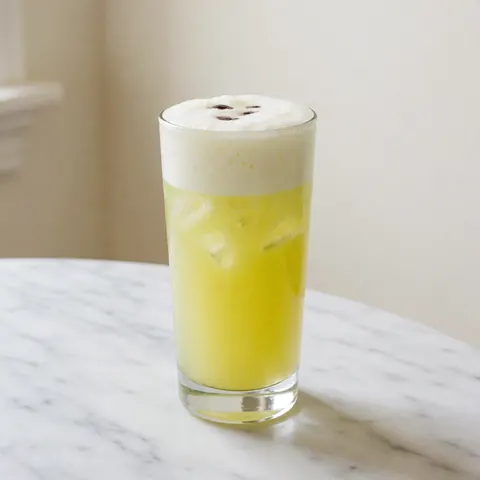 Pisco sour cocktail with white foam and bitters drops in a tall glass on a marble table, ideal for a cevicheria.