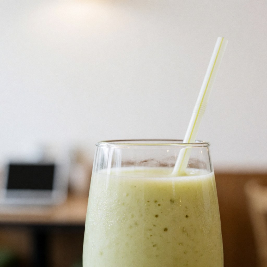A creamy green beverage served in a glass with a straw against a plain white wall in a restaurant setting